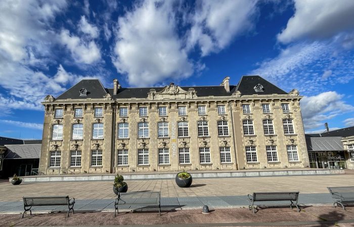 Bâtiment de la Médiathèque Intercommunale des Vosges avec un grand ciel bleu et des nuages blancs