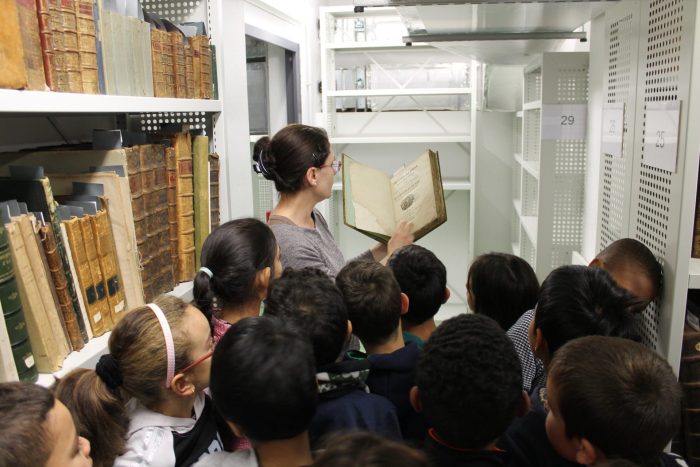 La responsable des archives montre un livre ancien aux enfants lors d’une visite scolaire