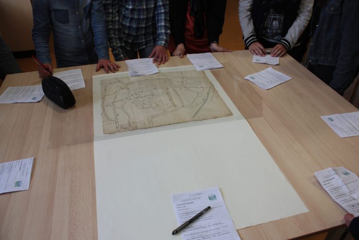 Élèves rassemblés autour d’une table observant une ancienne carte dans la salle de lecture des archives